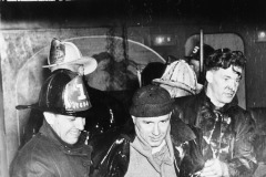 Fireman escort a man out of a New York building outside which hangs a banner reading \'Happy New Year\'. New York, 1941. By Weegee (Arthur Fellig).